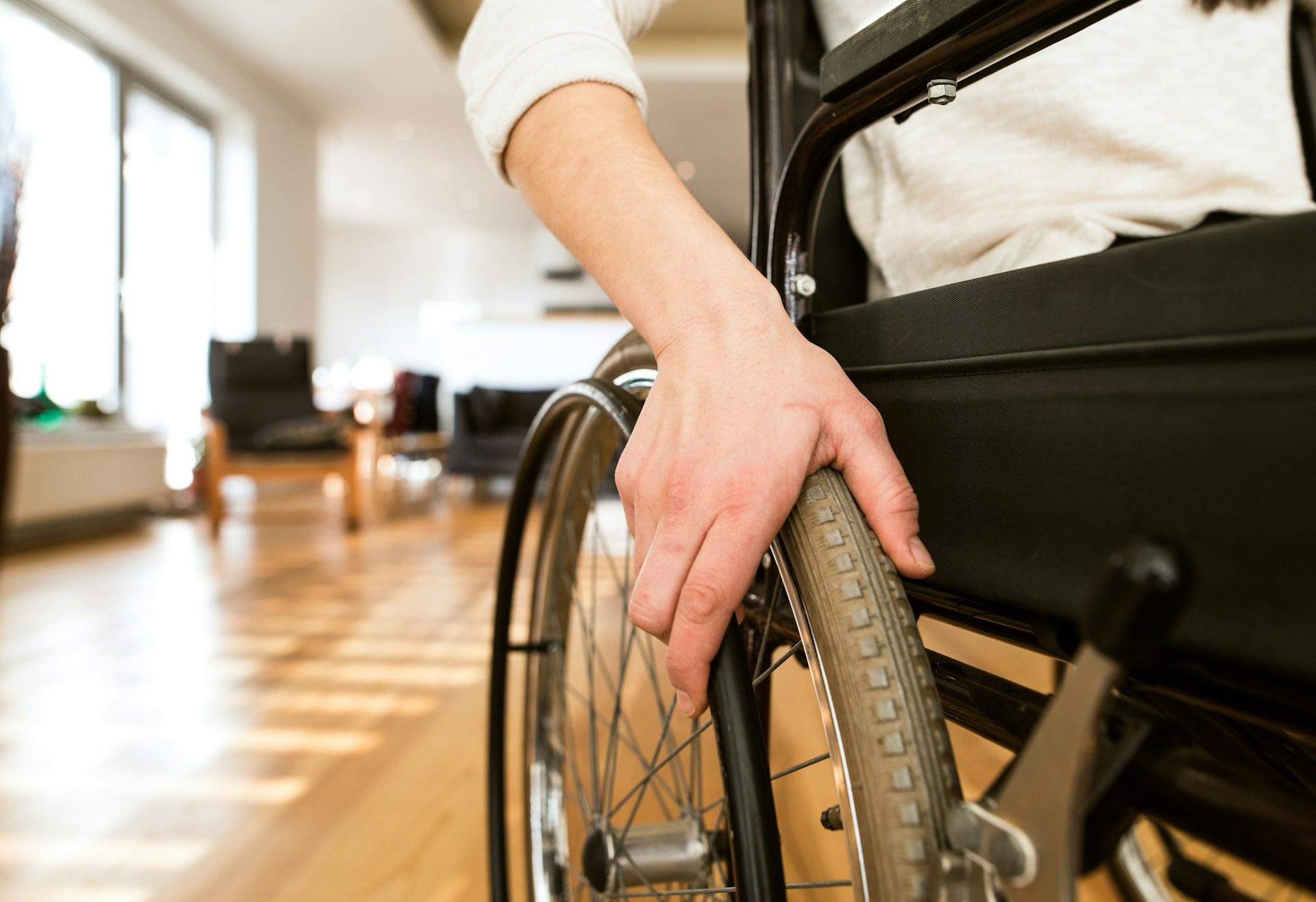 a person sitting in a wheelchair, the view is focused on their hand as it rests on one of the wheels