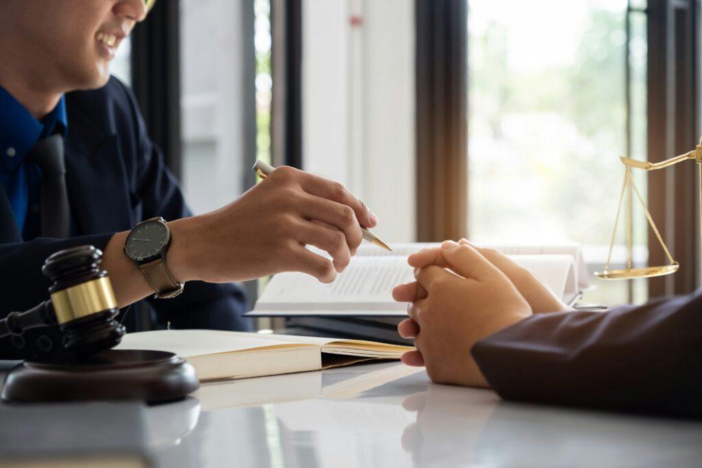 two people sitting at a desk, both wearing suits and one with a pen in his hand