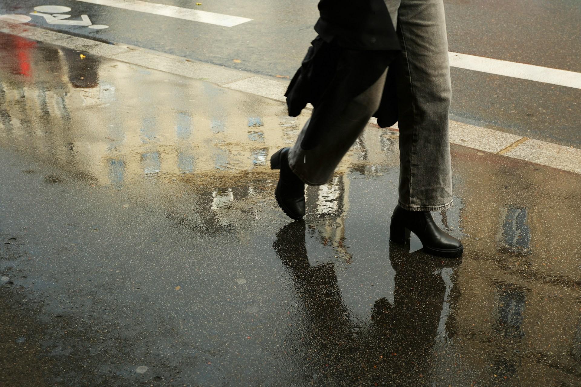 a closeup of a woman's shoes as she crosses a wet road