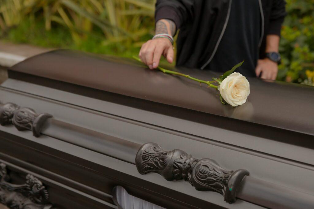 a person laying a white rose on a casket