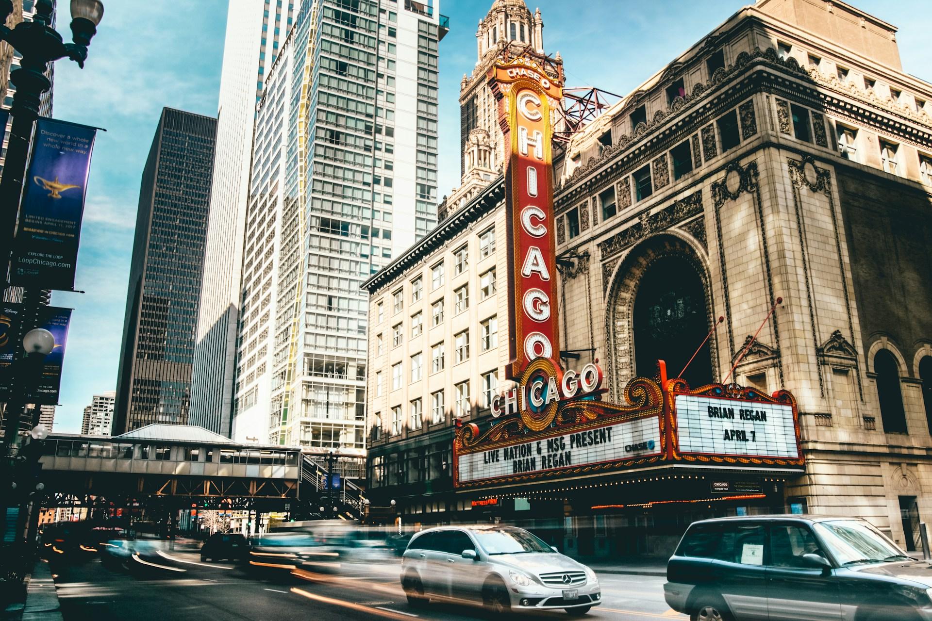 a street in chicago where cars are seen speeding in the foreground while a theater building looms in the back