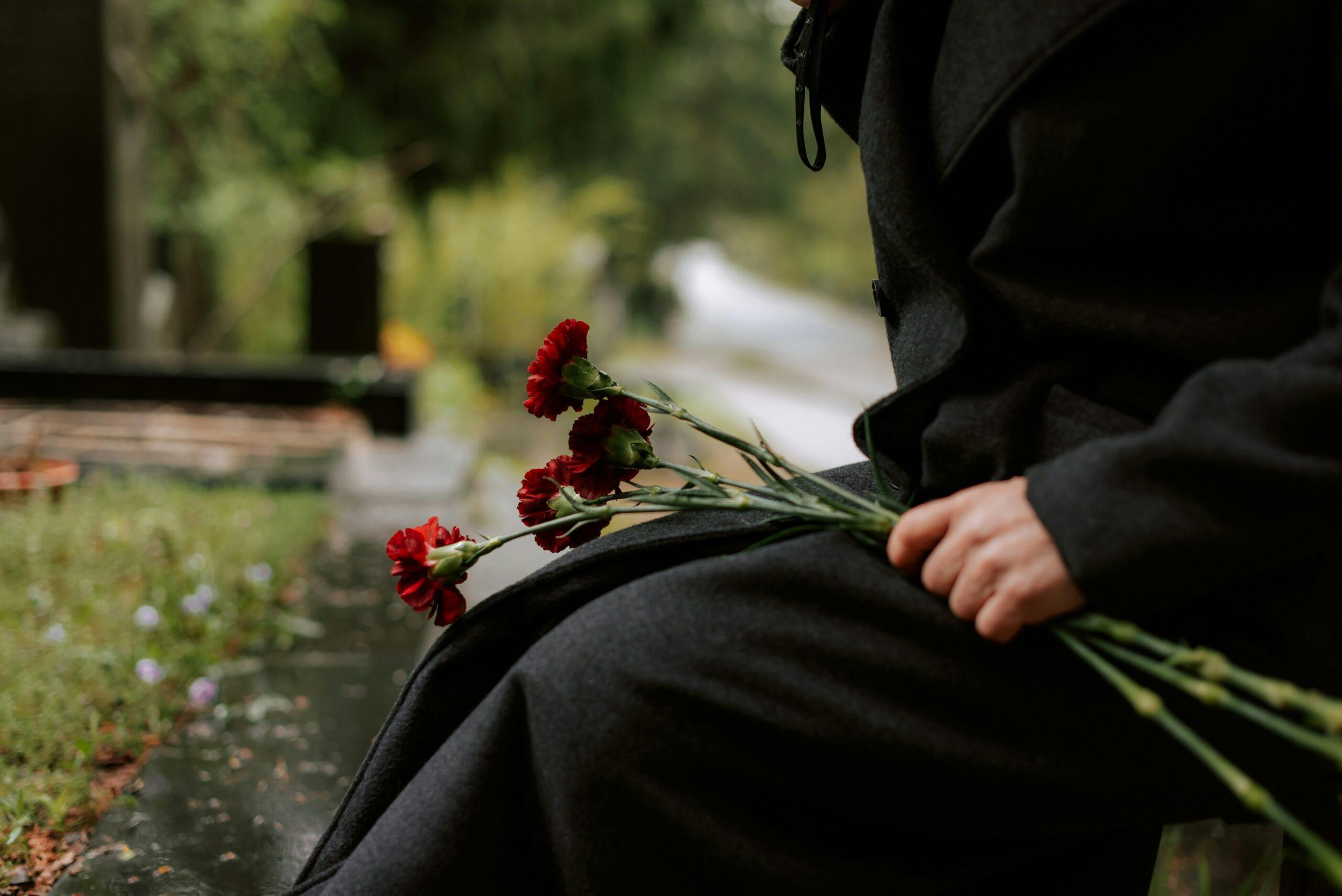 Person dressed in black sitting at a gravesite holding red carnations, symbolizing mourning and remembrance after a wrongful death.