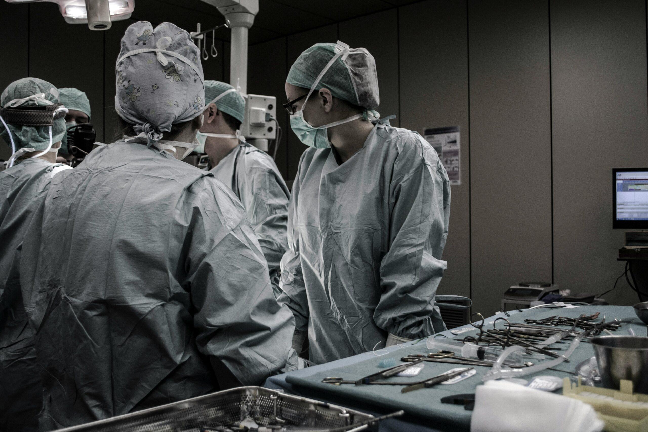 A team of surgeons in full protective gowns, masks, and caps gathered in an operating room, with surgical instruments laid out on a sterile table in the foreground.