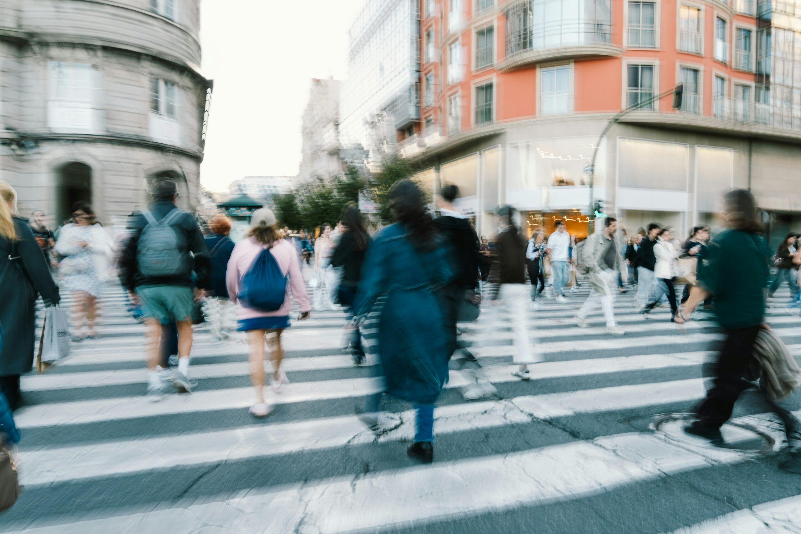Blurred image of several people crossing a street, creating a sense of movement and urban activity.