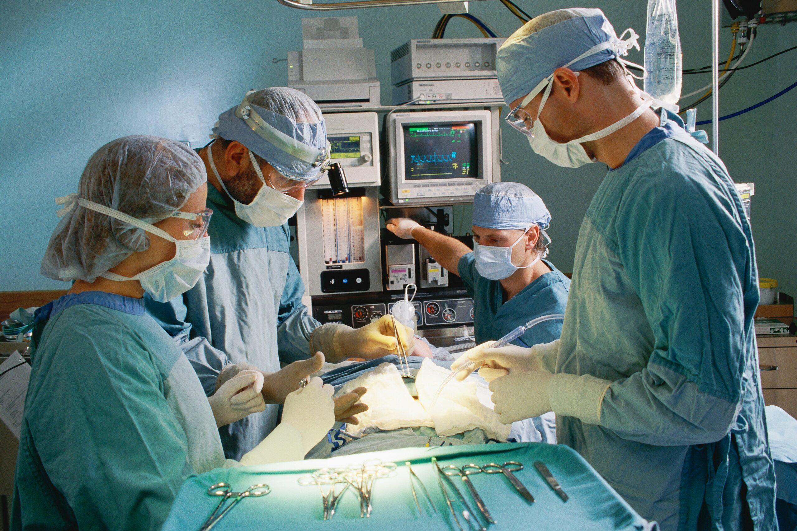 four doctors focused on a surgical patient. We cannot see the patient's face. All four doctors are in scrubs and masks