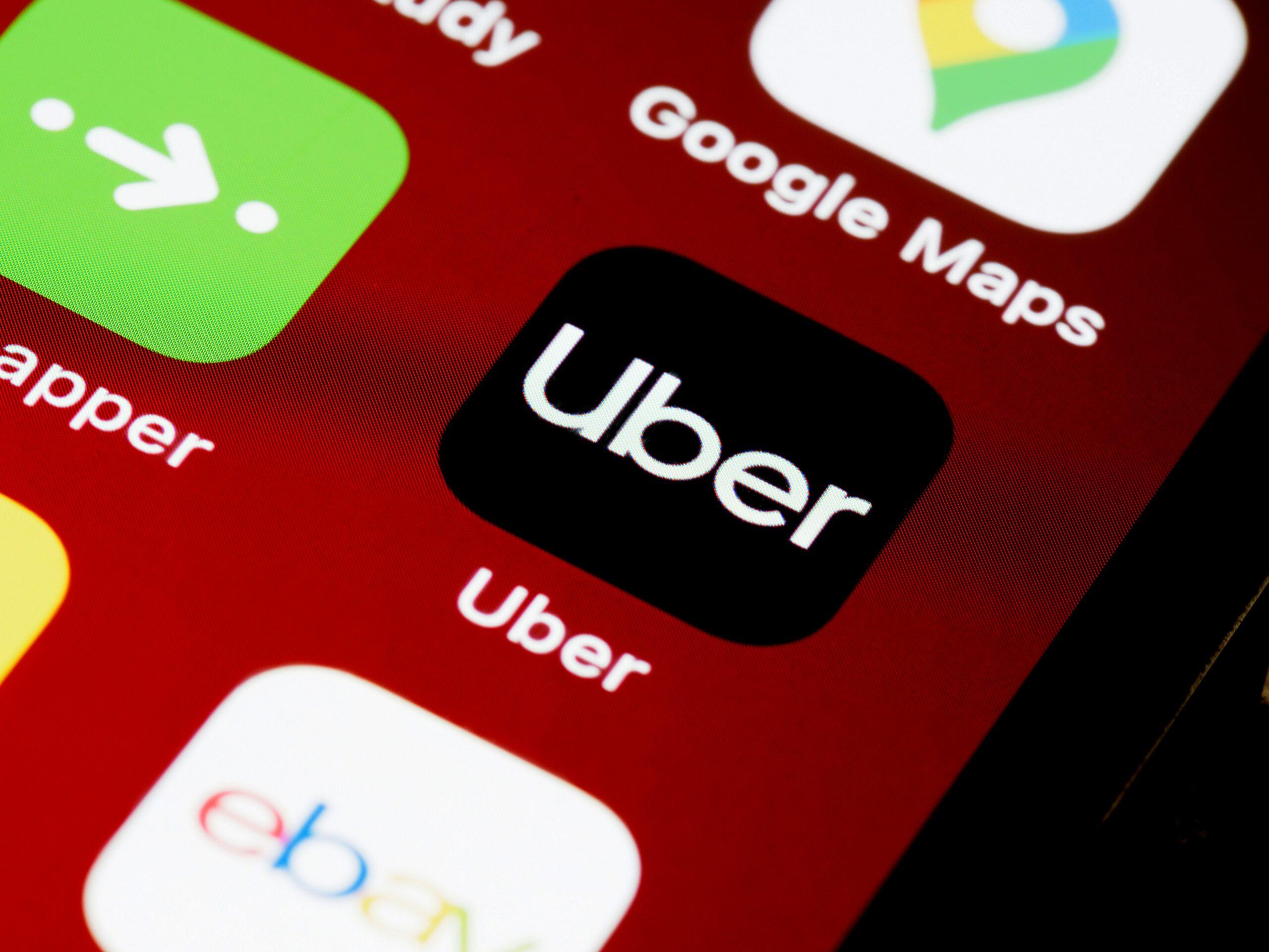 A smartphone screen with the Uber app prominently displayed on a maroon wallpaper.