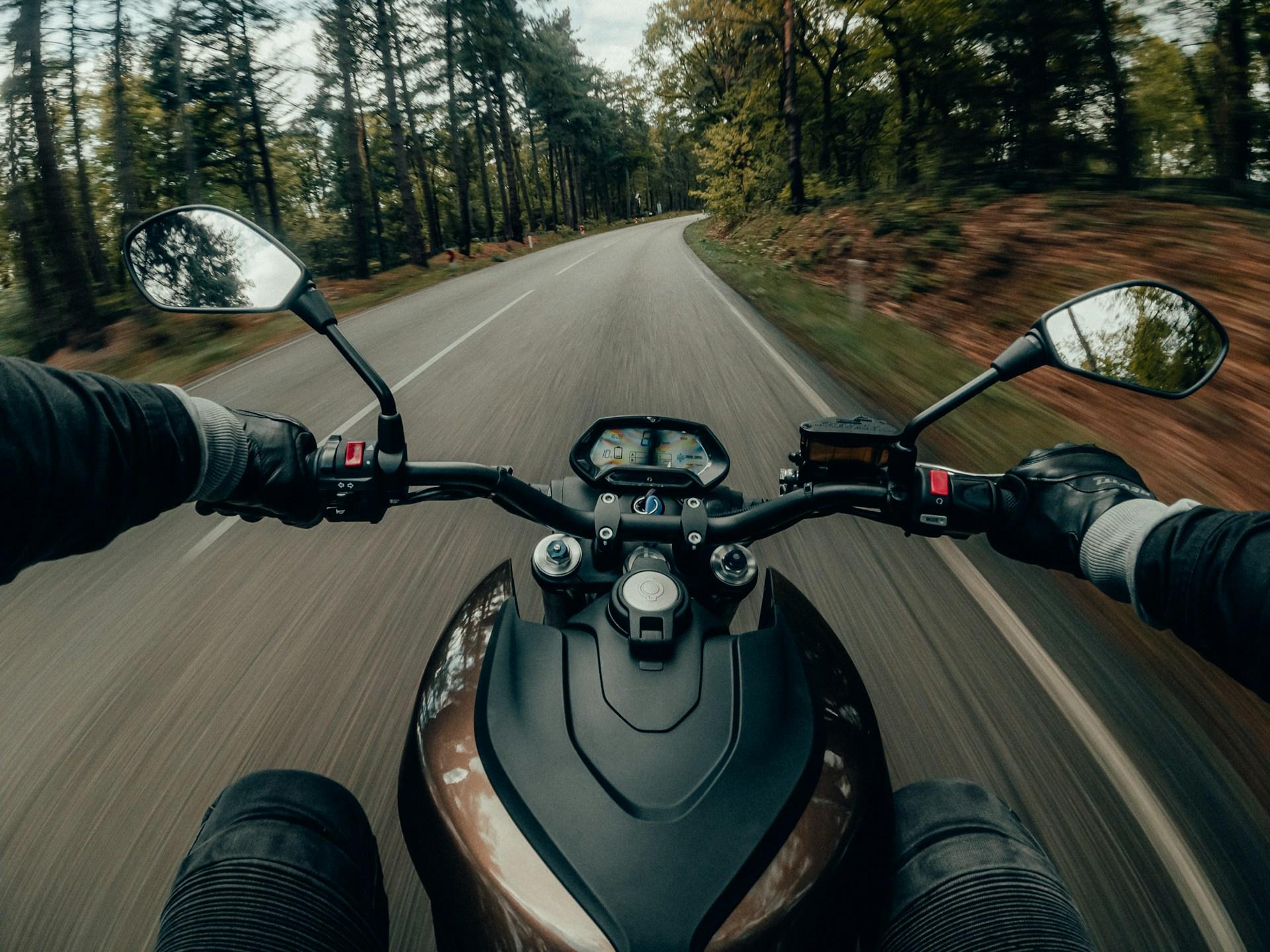 A person riding a motorcycle on a road in Cicero, surrounded by trees and clear blue skies.