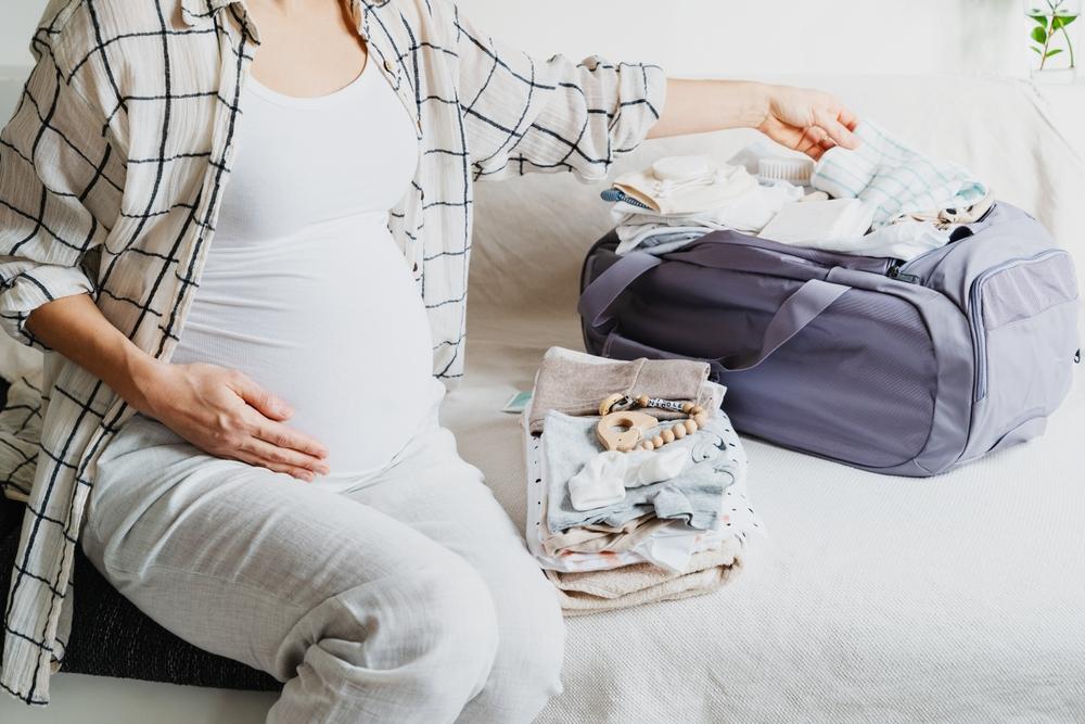 Pregnant woman packing baby clothes into a hospital bag